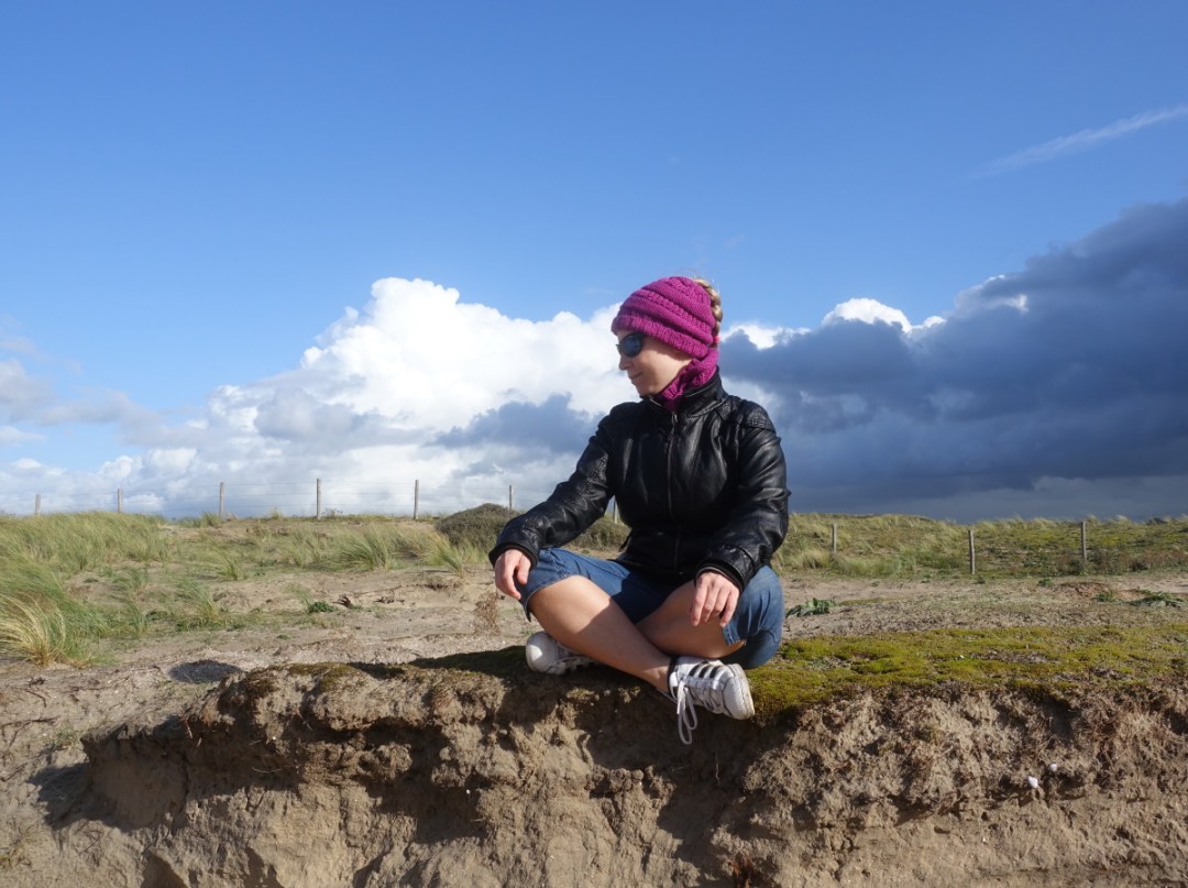 Lizzi im Schneidersitz auf Natursteinen. Links blauer Himmel und weiße Wolken. Rechts dunklere Regenwolken.