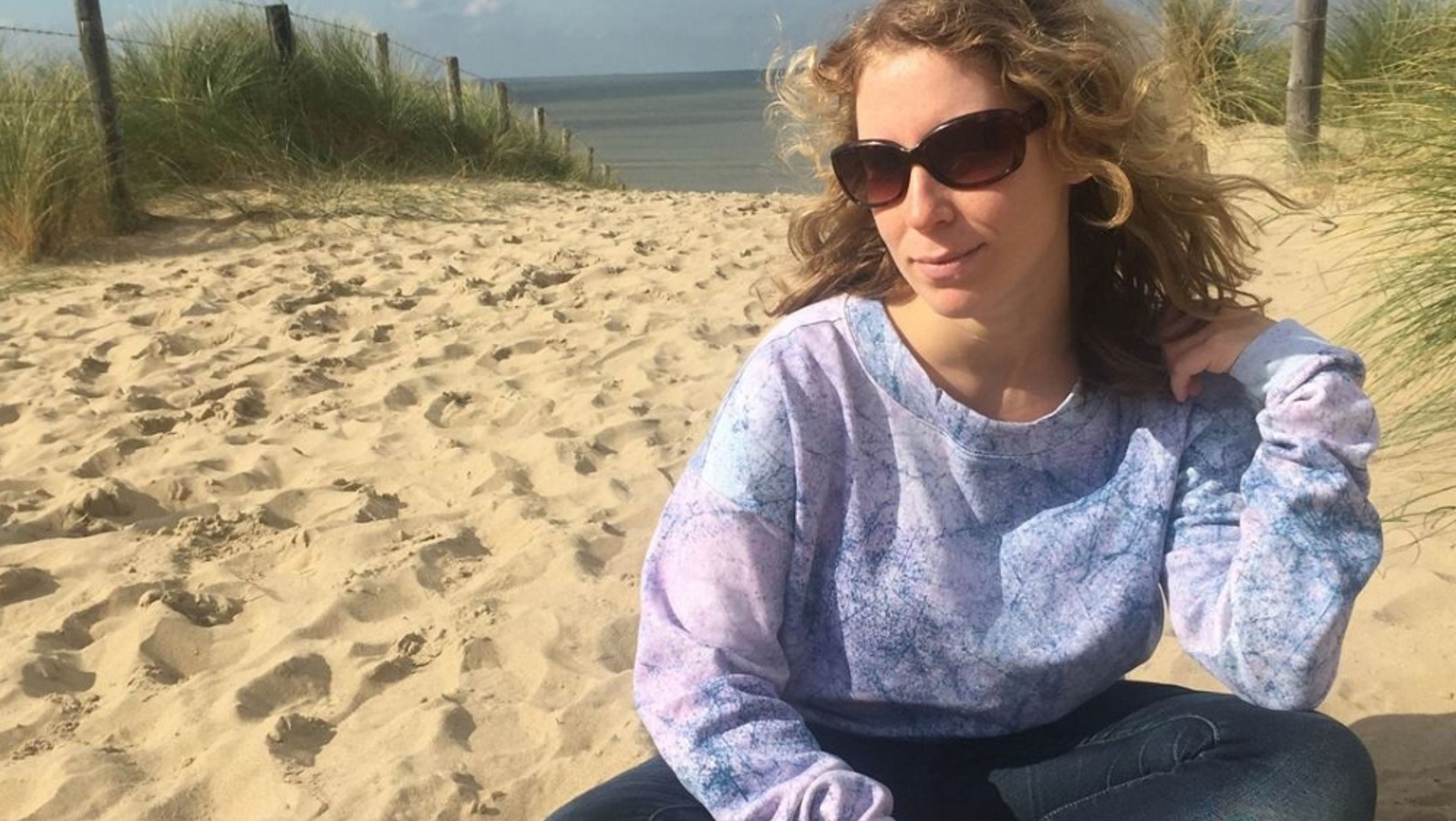 Lizzi sitzt im Schneidersitz im hellen Zandvoorter Dünensand mit dem Meer im Rücken.