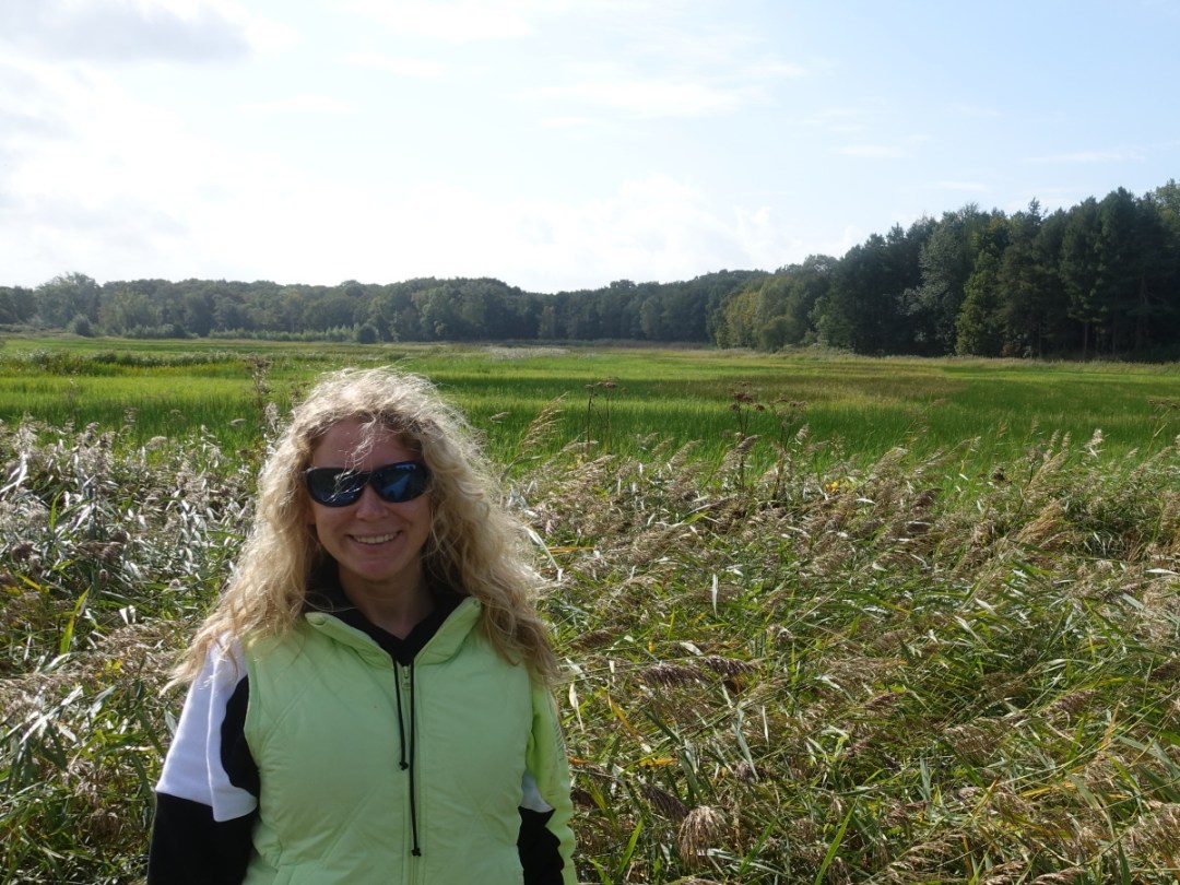 Lizzi lächelnd mit Gletscherbrille vor einem weiten Feld in der Sonne